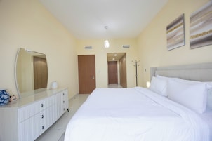 Habitación de hotel con una cama grande, cómoda, espejo, perchero y una puerta que da a otra habitación.