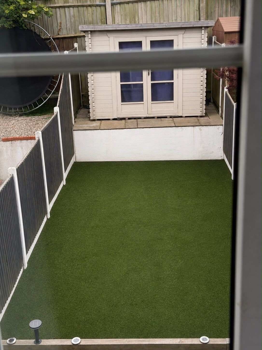 Une cour arrière clôturée avec une pelouse artificielle, un petit abri de jardin et une clôture en bois.
