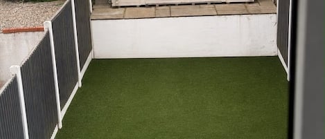 A fenced backyard with artificial grass, a small shed, and a wooden fence.
