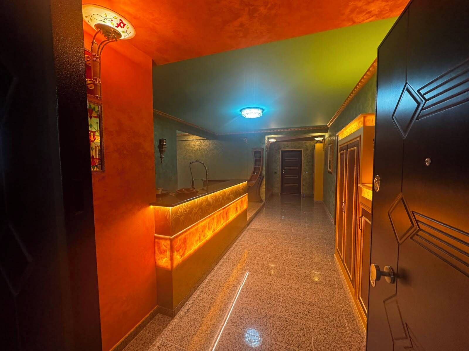 A hotel hallway with a reception desk, a mirror, a door, and a light fixture.