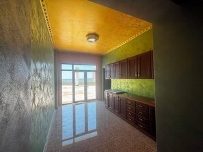A room with a large sliding glass door leading to an outdoor area, a kitchen with dark wooden cabinets, and a textured yellow ceiling. - Luxury Apartament with an amazing seaview (Golem)