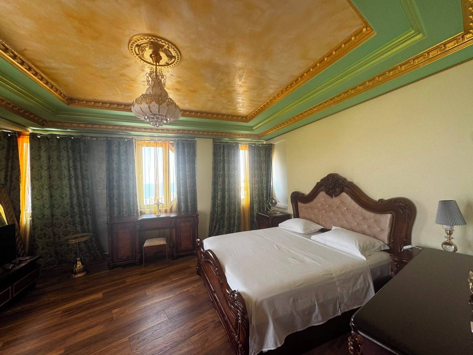 A room with a large bed, a desk, a chair, a lamp, and a window with curtains.