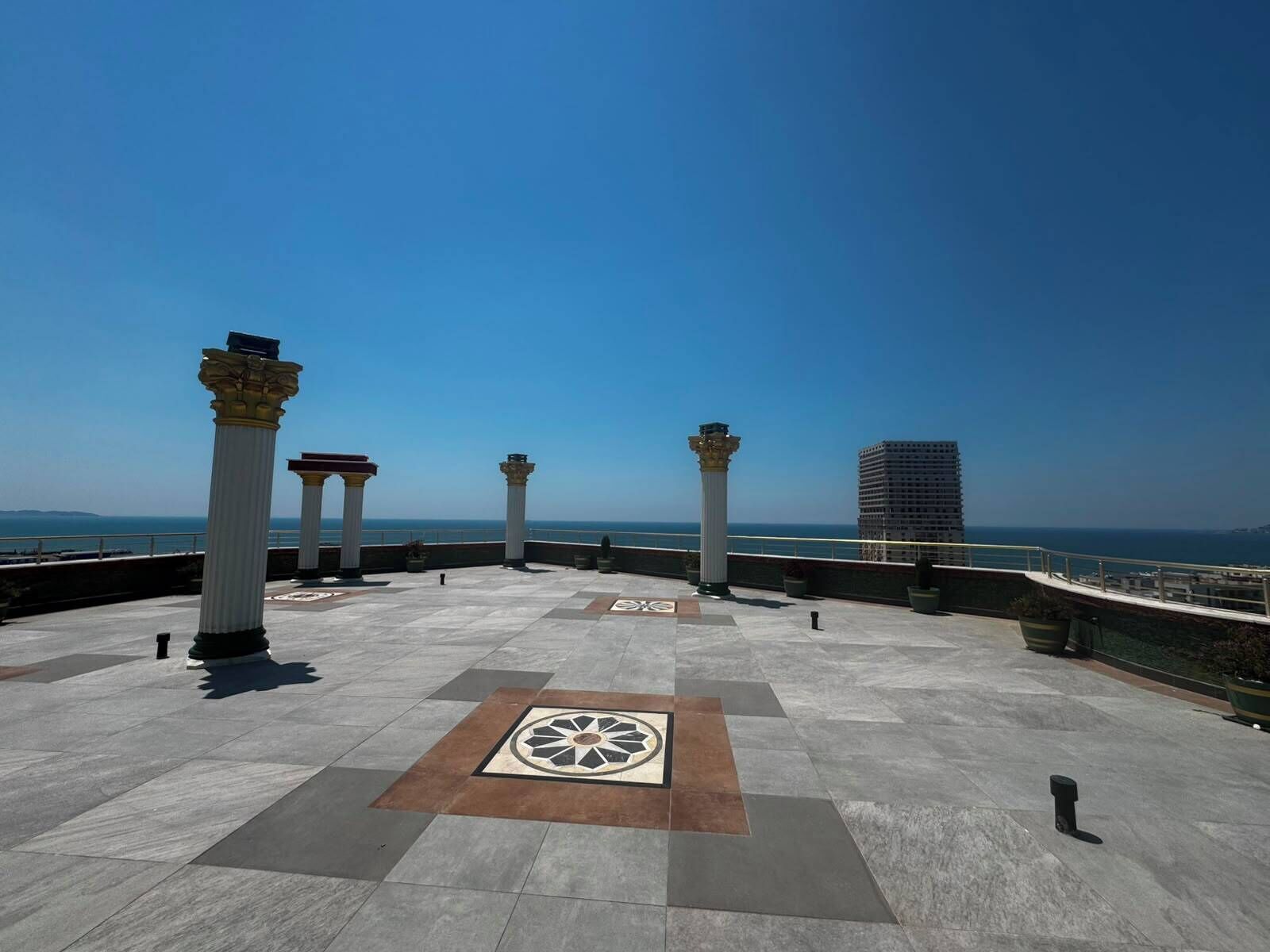 A rooftop terrace with columns, a patterned floor, and a view of the sea.