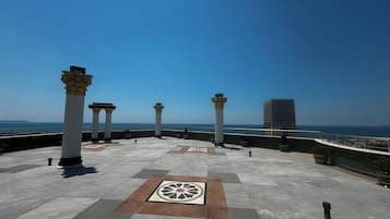 A rooftop terrace with columns, a patterned floor, and a view of the sea.