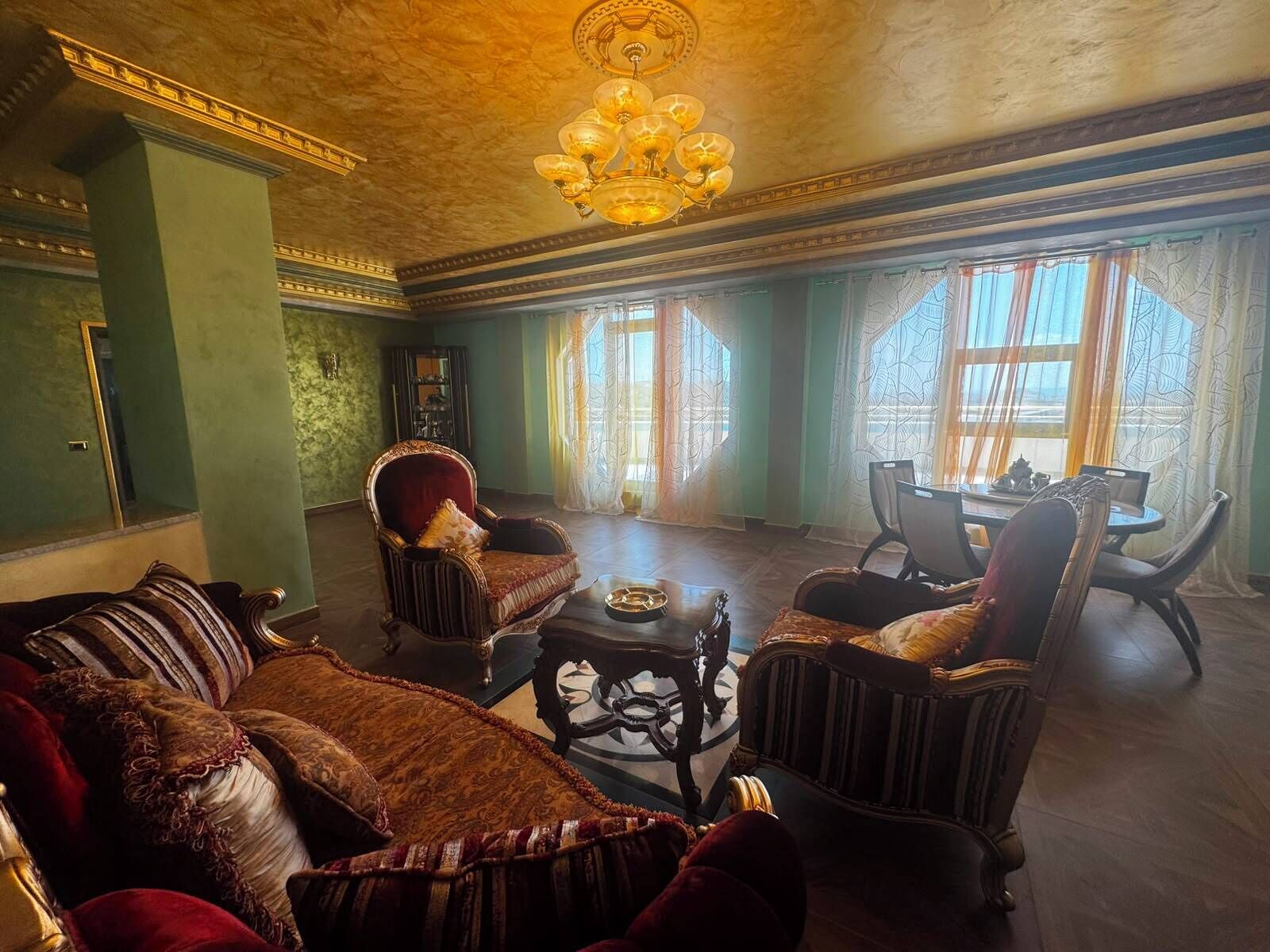 A room with a sofa, armchairs, a chandelier, and a dining table with chairs.