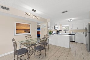 A modern kitchen with white cabinetry, a central island, and a dining area with a glass table and metal chairs.