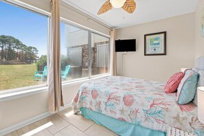 A bedroom with a large window, a bed with floral bedding, a flat-screen TV, and a framed informational poster on the wall.