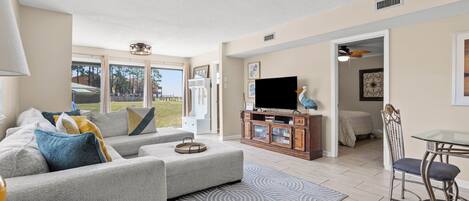 A modern living room with a grey sofa, a flat-screen TV, and a dining area with a table and chairs.