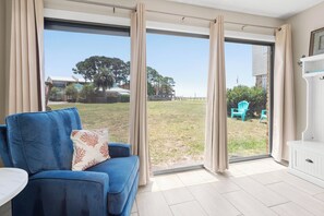 A room with a blue sofa, a white cabinet, and a view of a grassy yard with trees and a building in the distance.