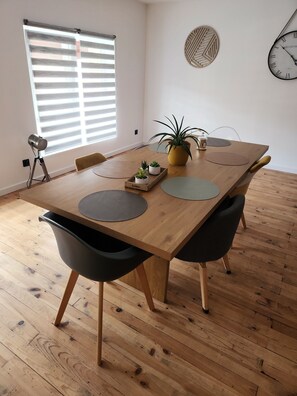 A modern dining area with a wooden table, black chairs, a potted plant, and a wall clock.