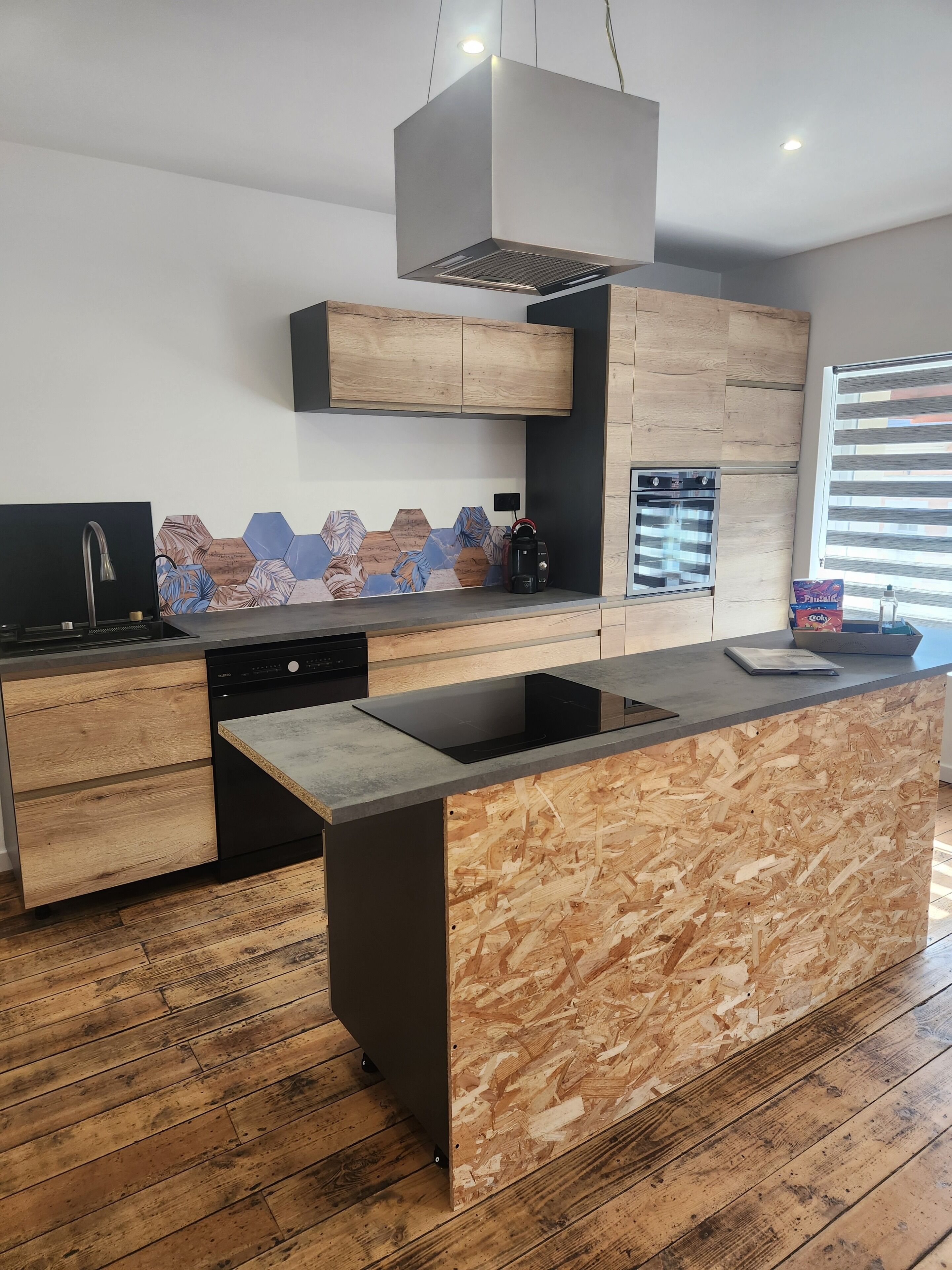 A modern kitchen with a central island, built-in appliances, and a wooden backsplash.