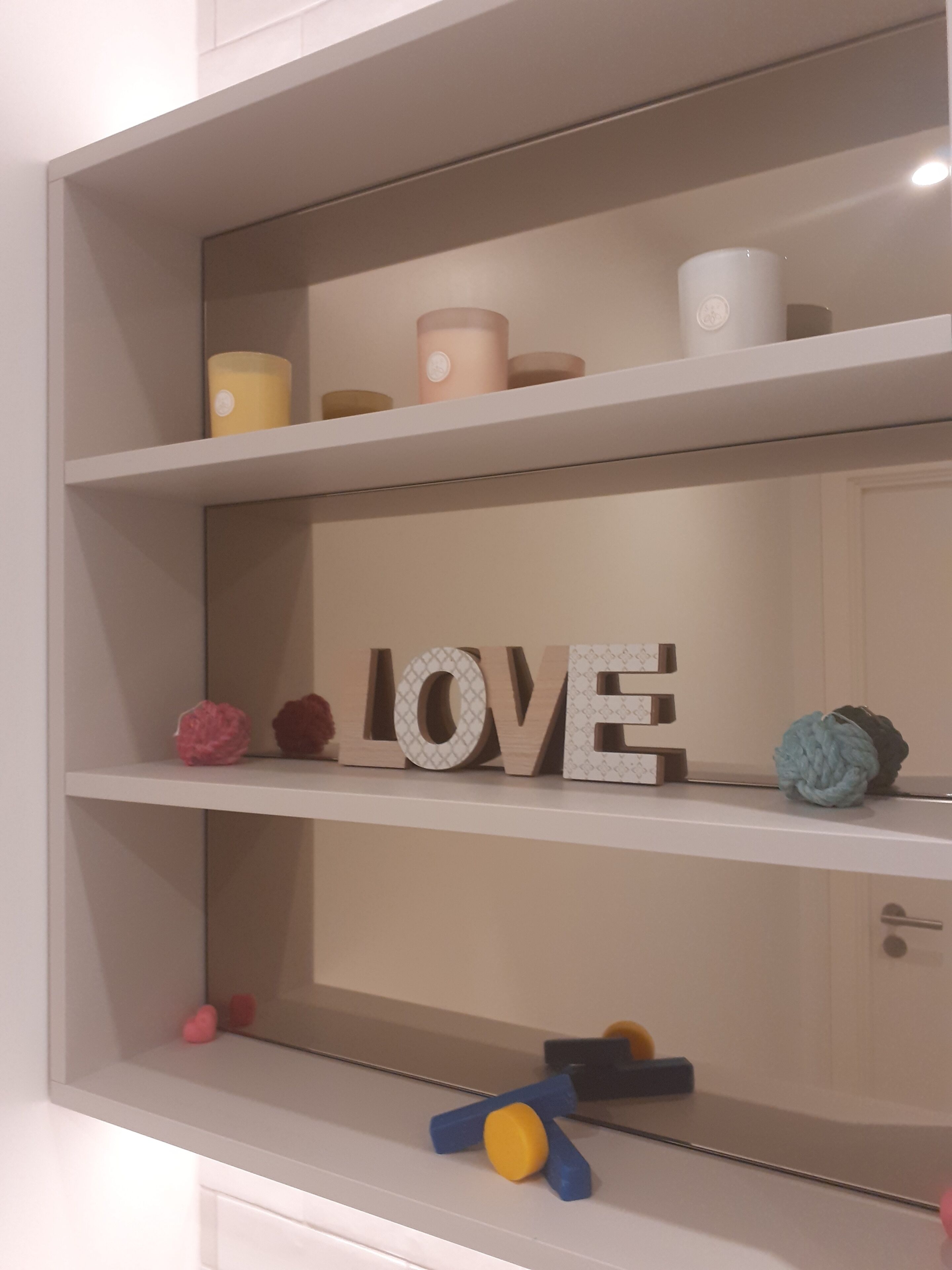 Una estantería con objetos decorativos, incluyendo un letrero grande con la palabra 'LOVE', velas y figuritas.