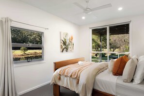 Un dormitorio con cama, ventana, ventilador de techo y un cuadro en la pared.