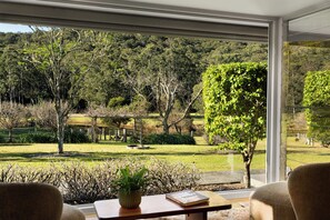 Una habitación con un amplio ventanal que da a un exuberante jardín y una colina arbolada.