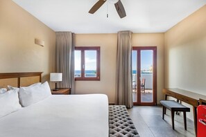 A hotel room with a bed, a desk, a chair, a bench, a ceiling fan, and a view of the sea through a door. - Casa Lucila Mazatlan Curamoria Collection (Mazatlán)