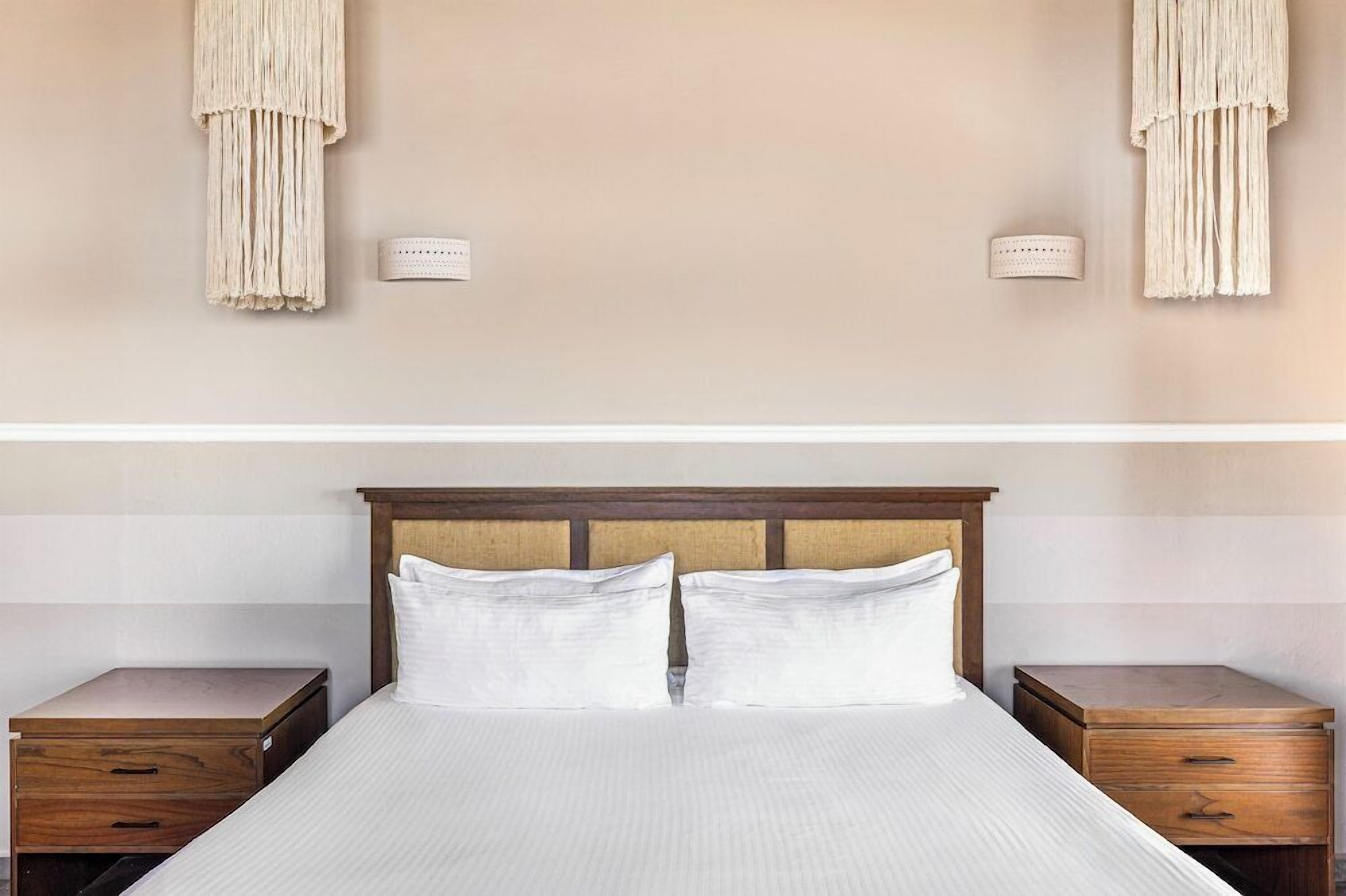 Una habitación de hotel con una cama, dos mesitas de noche y lámparas de pared.