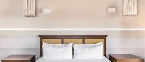 Una habitación de hotel con una cama, dos mesitas de noche y lámparas de pared.
