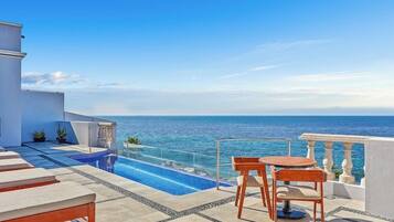 A rooftop pool area with a clear view of the sea, a small table and two chairs, and a modern architectural design.