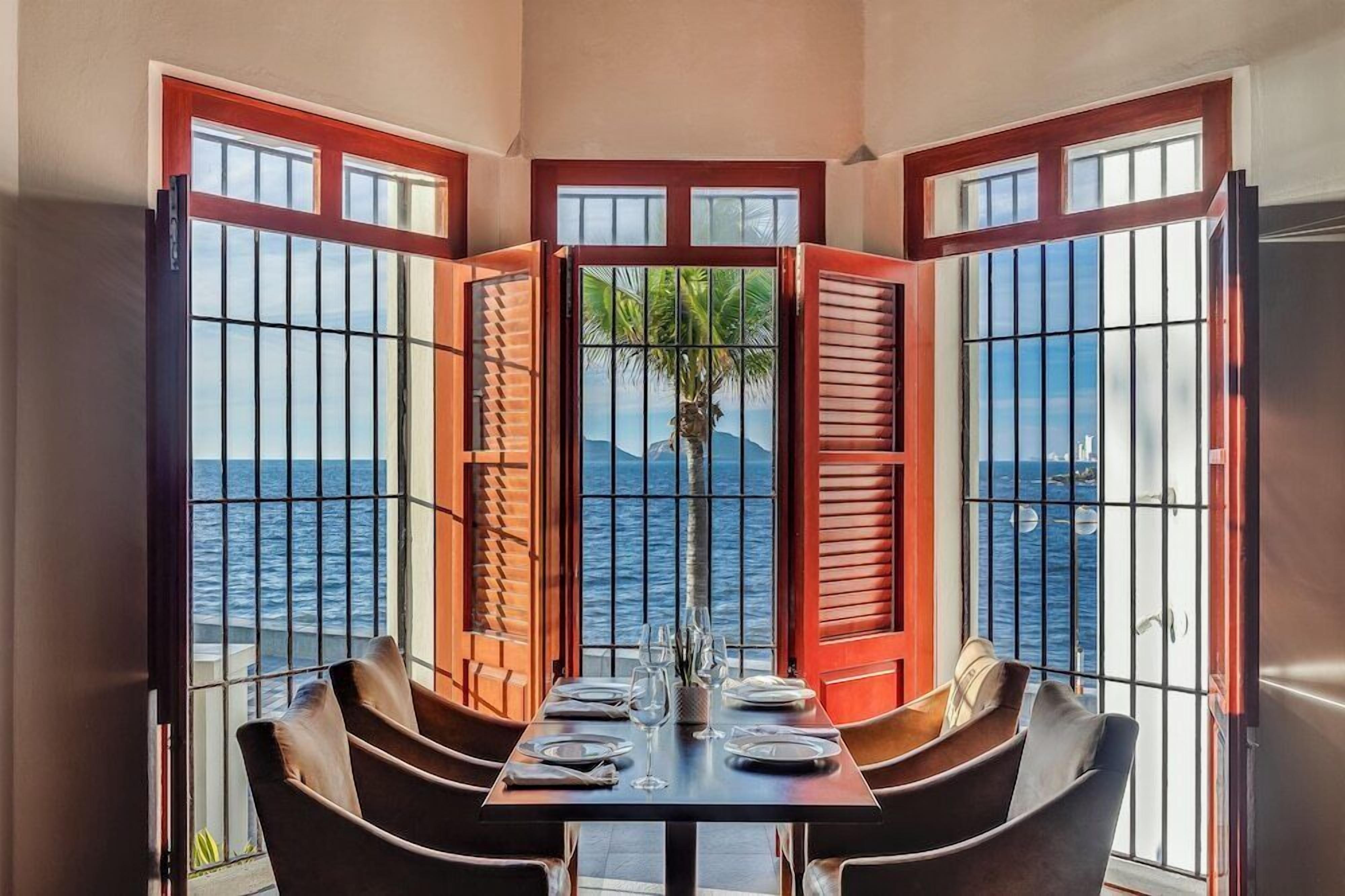 A dining area with a table set for four, overlooking a body of water through a window with metal bars.