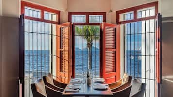 Comedor con una mesa dispuesta para cuatro, con vista a una masa de agua a través de una ventana con rejas.