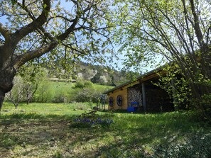 A rustic wooden cabin with a stone wall, surrounded by lush greenery and flowering plants. - Renovated farmhouse, panoramic view - guests (Vorey)