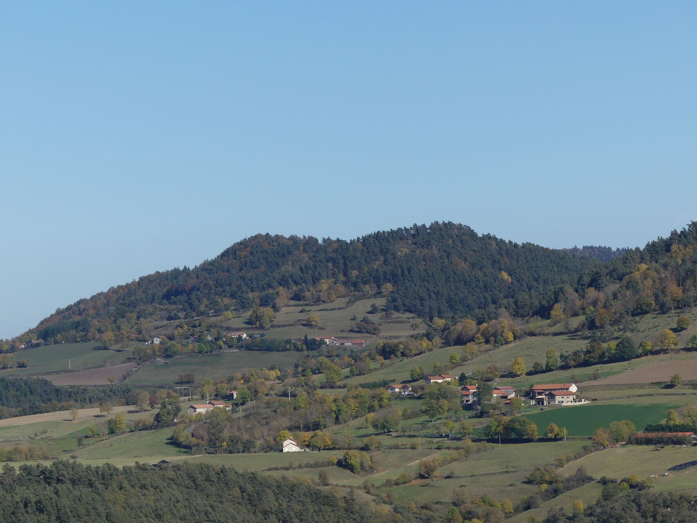 A rural landscape with rolling hills, scattered houses, and a clear sky.