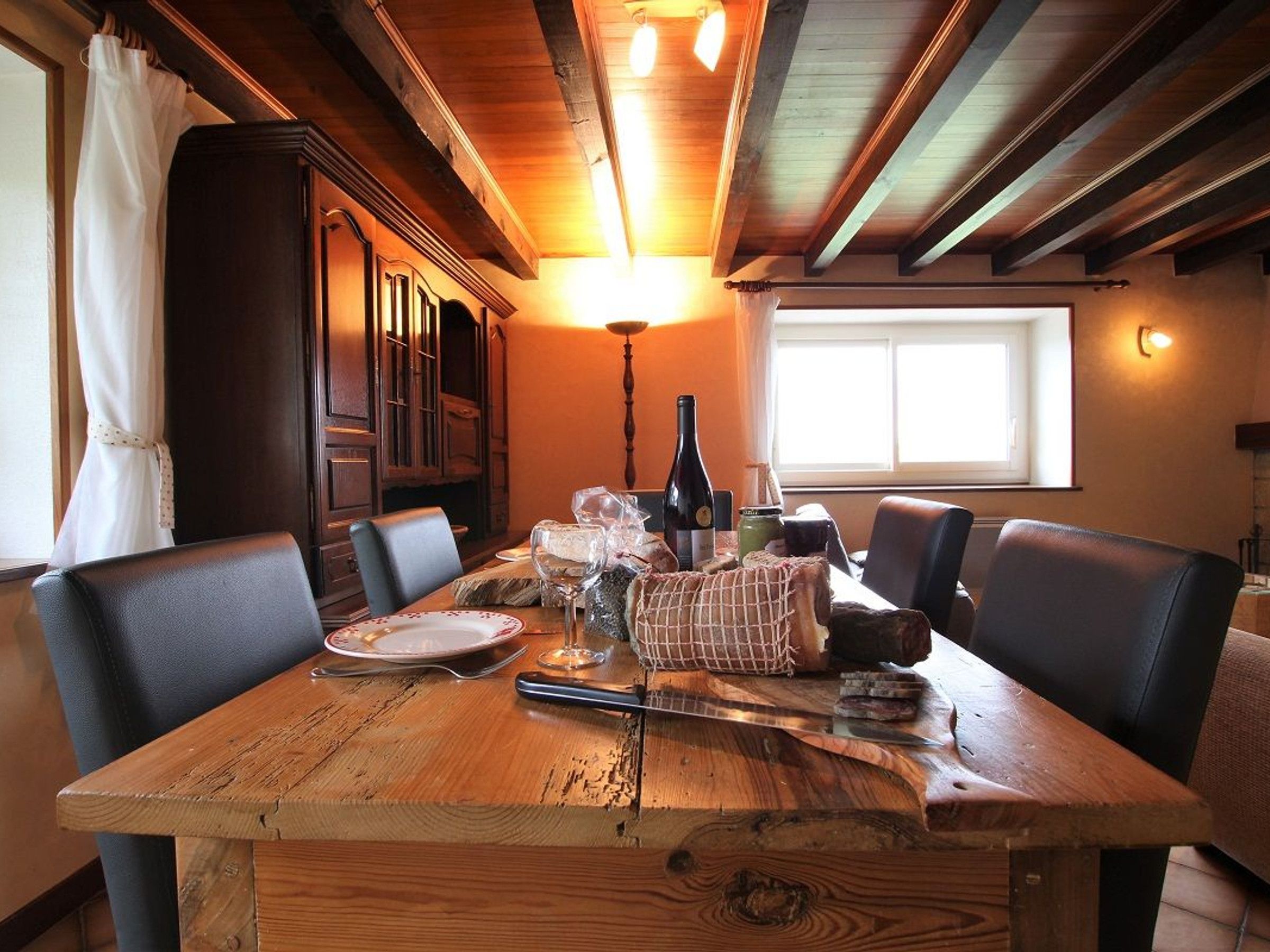A wooden dining table with chairs, a wine bottle, and a candle.