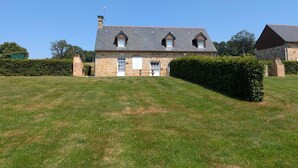 A stone house with a sloped roof, two chimneys, and a small front porch. - Cozy house, pets allowed - 5 guests (Saint-Georges-de-Rouelley)