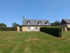Ein Steinhaus mit geneigtem Dach, zwei Schornsteinen und einer kleinen Veranda.