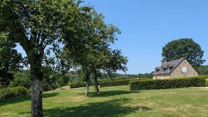 A stone house with a sloped roof, surrounded by a well-maintained lawn and hedges. - Cozy house, pets allowed - 5 guests (Saint-Georges-de-Rouelley)