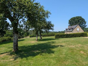 Ein Steinhaus mit geneigtem Dach, umgeben von einem gepflegten Rasen und Hecken.