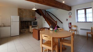 A spacious kitchen with a stone wall, a wooden staircase, and a dining area with wooden furniture. - Cozy house, pets allowed - 5 guests (Saint-Georges-de-Rouelley)