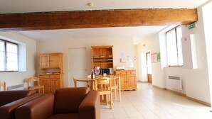 A spacious room with a wooden ceiling, a dining area with a table and chairs, and a kitchenette with cabinets and appliances. - Cozy house, pets allowed - 5 guests (Saint-Georges-de-Rouelley)