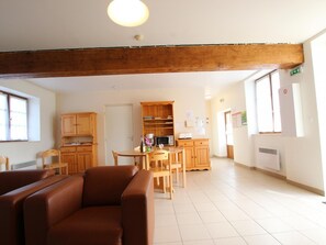 Ein geräumiger Raum mit Holzbalkendecke, einer Essecke mit Tisch und Stühlen sowie einer Küchenzeile mit Schränken und Geräten.