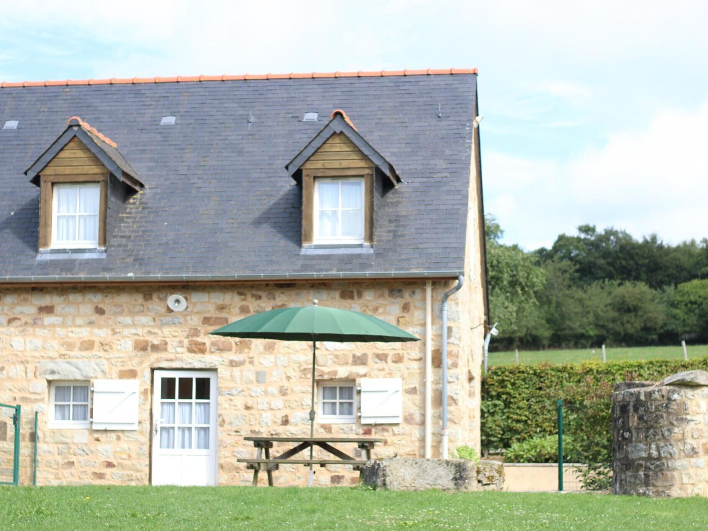 A stone building with two windows, a door, and a picnic table with an umbrella.