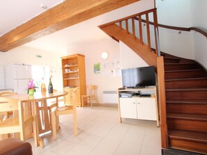 Eine Küche mit Holzschränken, einem Esstisch mit Stühlen, einem Fernseher auf einem Schrank und einer Holztreppe.