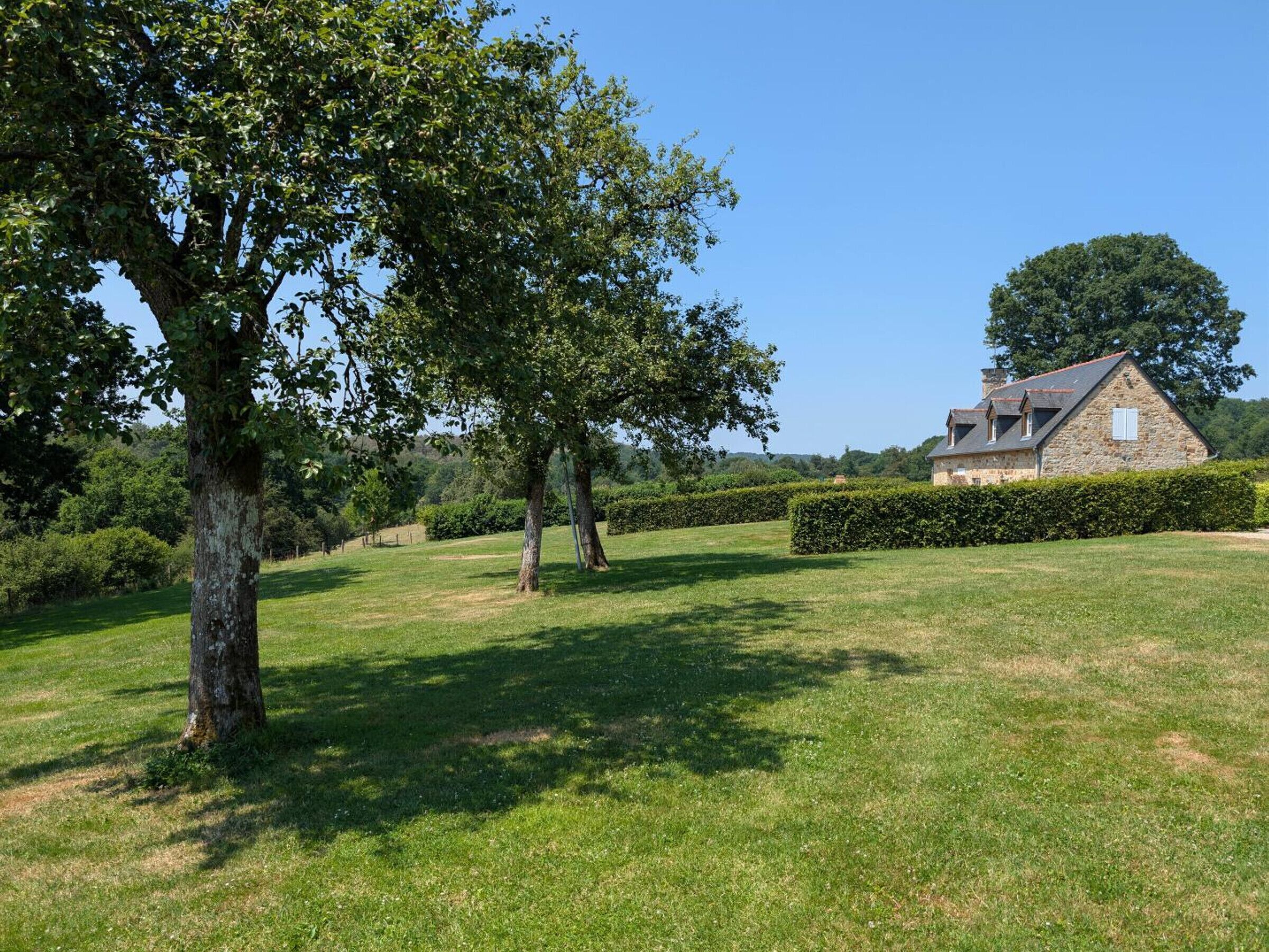 A stone house with a sloped roof, surrounded by a well-maintained lawn and hedges.