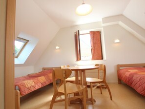 Ein kleiner, gemütlicher Raum mit schrägen Wänden, einem Oberlicht, einem Tisch mit Stühlen und zwei Betten mit passenden Bettdecken.