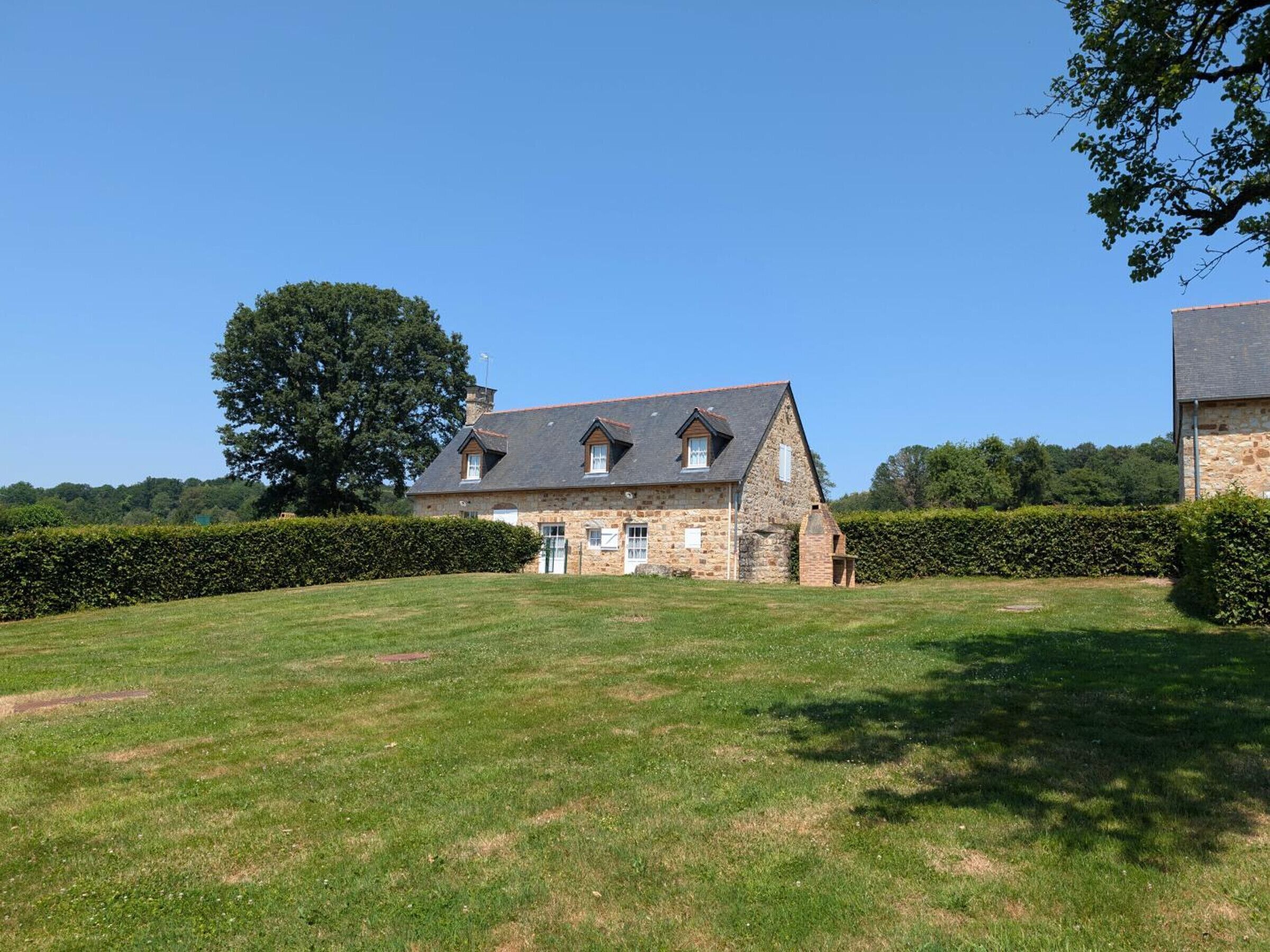 A stone house with a sloped roof, surrounded by a well-maintained lawn and a hedge.