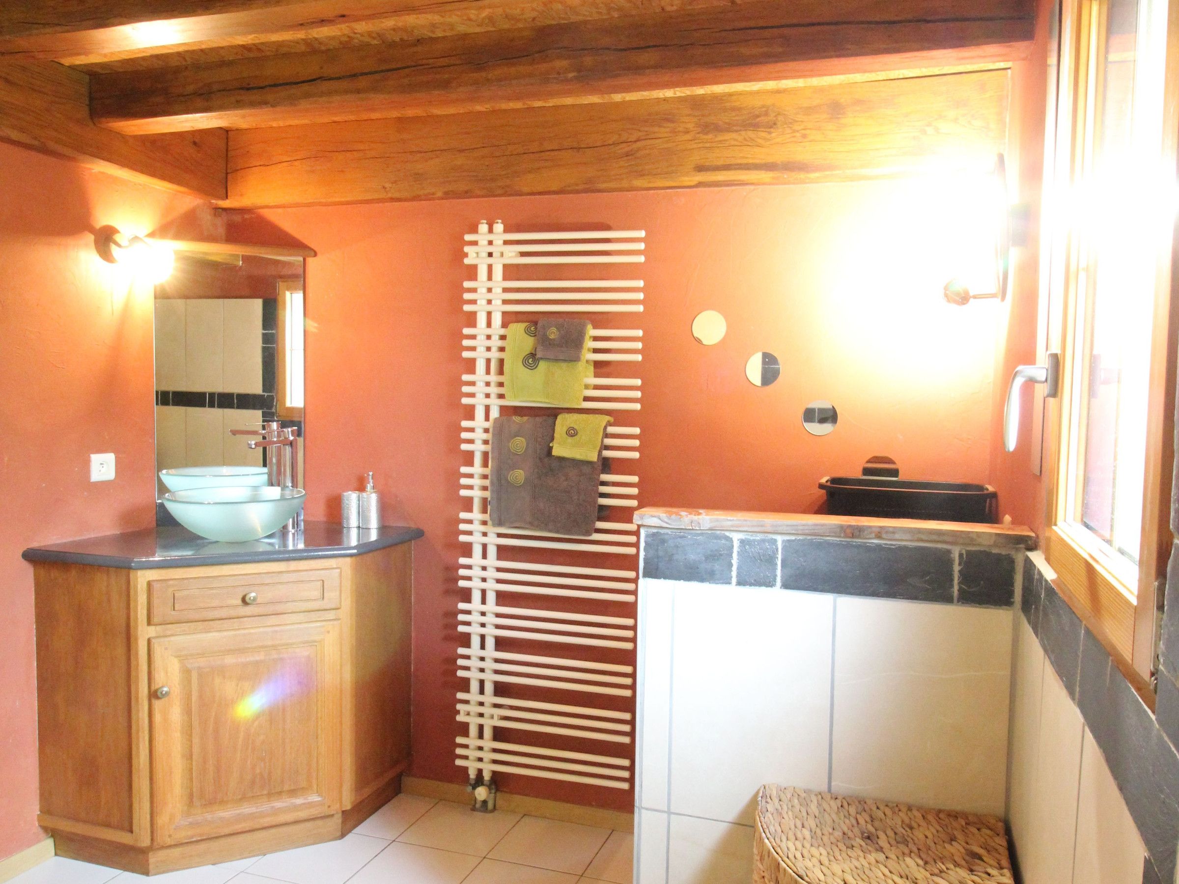 Un baño con tocador de madera, lavamanos de vidrio, barra para toallas y zona de ducha con azulejos.