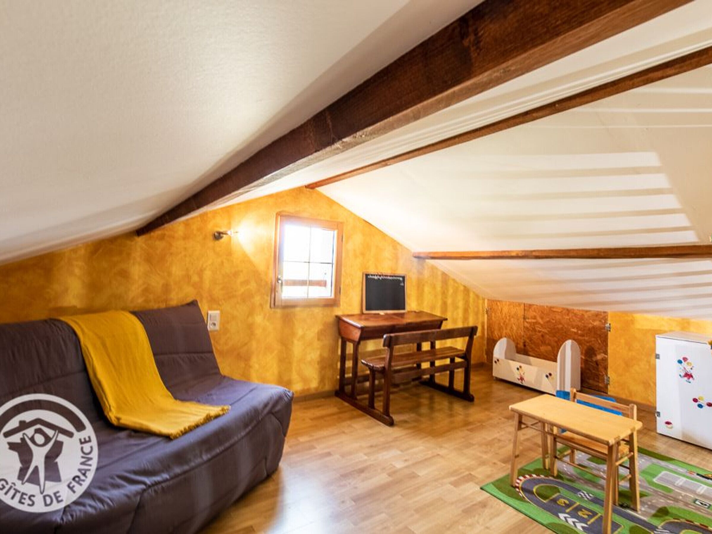 Une pièce mansardée accueillante, avec un canapé, une petite table, un banc en bois et un tapis de jeu pour enfants.