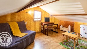 Ein gemütliches Dachzimmer mit einer Couch, einem kleinen Tisch, einer hölzernen Bank und einer Kinderspielecke.
