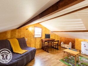 Ein gemütliches Dachzimmer mit einer Couch, einem kleinen Tisch, einer hölzernen Bank und einer Kinderspielecke.