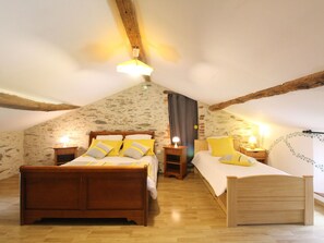 Ein Schlafzimmer mit geneigter Decke, Holzbalken, einem Bett mit Holzrahmen, zwei Nachttischen mit Lampen und einem kleinen Holzhocker.