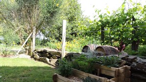 Ein Garten mit einem hölzernen Pflanzkasten, einem rustikalen Fass und einem Holzpfosten.
