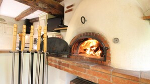 Ein Backofen für Pizza mit Feuer im Inneren, Holz-Pizza-Schaufeln hängen an der Wand und eine Ziegelregal befindet sich darunter.