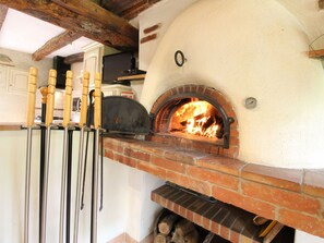Ein Backofen für Pizza mit Feuer im Inneren, Holz-Pizza-Schaufeln hängen an der Wand und eine Ziegelregal befindet sich darunter.