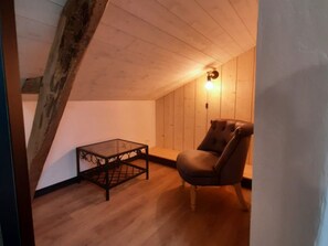 Ein Zimmer mit schrägen Wänden, einem Tisch, einem Stuhl und einer Wandleuchte.