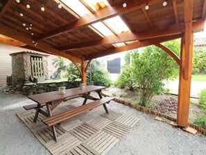 Eine hölzerne Pergola im Freien mit einem Picknicktisch, umgeben von Kies und Pflanzen.