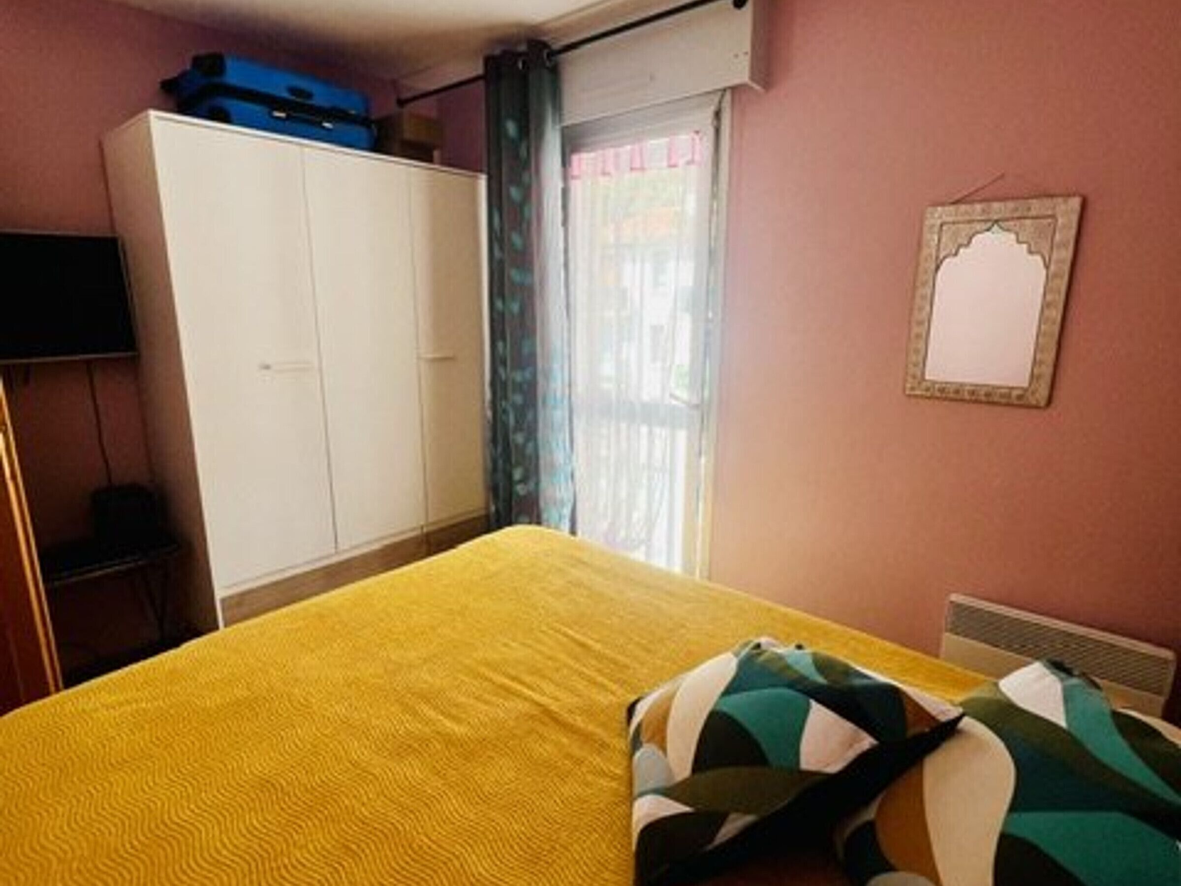 Una habitación con cama, armario, televisor y ventana con cortinas.